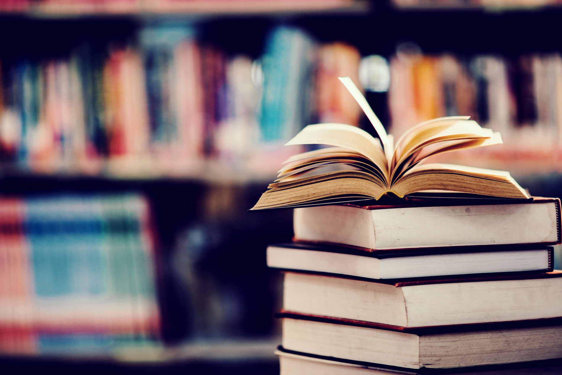 Una pila de libros frente a una biblioteca.